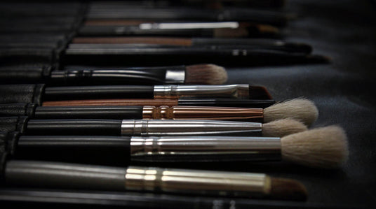 Eine Nahaufnahme mehrerer Make-up-Pinsel mit schwarzen und metallischen Griffen, die ordentlich auf einer dunklen Oberfläche angeordnet sind.