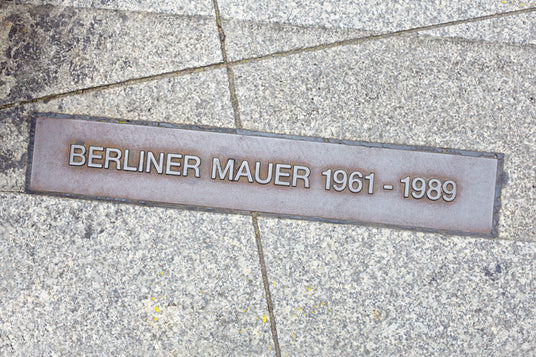 Auf einer in den Straßenbelag eingelassenen Gedenktafel steht „BERLINER MAUER 1961–1989“ und markiert den ehemaligen Verlauf der Berliner Mauer.