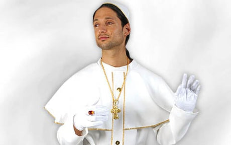 Eine Person in weißer religiöser Kleidung mit einer goldenen Kreuzkette, weißen Handschuhen und einer weißen Kappe, die vor einem schlichten weißen Hintergrund steht.