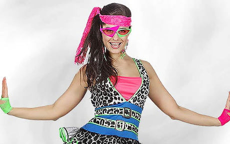 Eine Person in einem farbenfrohen, von den 1980er Jahren inspirierten Kostüm mit Animal-Print, Neon-Accessoires und einem rosa Stirnband, die mit ausgestreckten Armen vor einem weißen Hintergrund posiert.