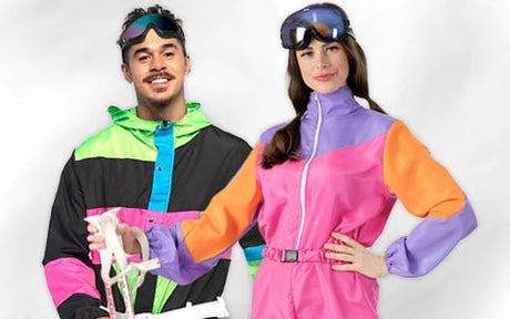 Zwei Personen in bunten Retro-Skianzügen und Skibrillen stehen nebeneinander vor einem schlichten Hintergrund, halten Skistöcke in den Händen und lächeln in die Kamera.