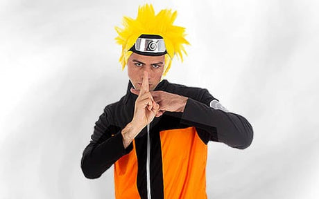 Eine Person in einem orange-schwarzen Kostüm mit einer gelben, stacheligen Perücke und einem Stirnband, die die Hände in einer aus Animes bekannten Geste hält.