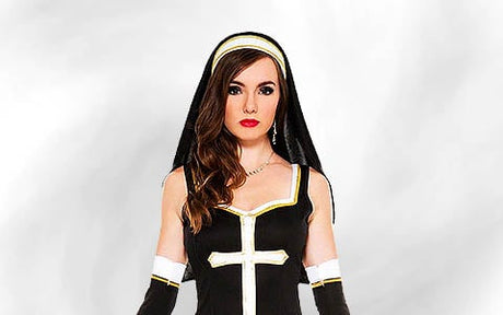 Eine Frau in einem schwarz-weißen Nonnenkostüm mit einem großen Kreuz auf der Vorderseite, die vor einem schlichten hellen Hintergrund posiert.
