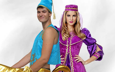 Zwei kostümierte Personen: ein Mann in einem blau-goldenen Dschinn-Kostüm und eine Frau in einem lila-goldenen Kleid im mittelalterlichen Stil mit Kopfschmuck, die nebeneinander vor einem hellen Hintergrund stehen.