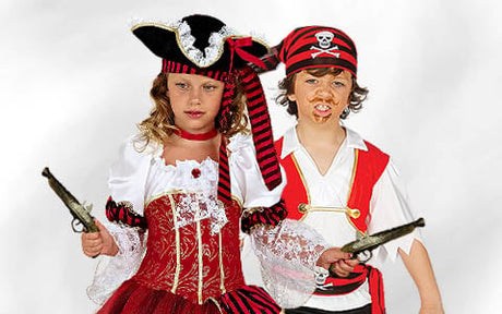 Zwei als Piraten verkleidete Kinder, das eine in einem rot-goldenen Kleid mit Hut, das andere in einem rot-weißen Hemd mit einem gestreiften Bandana; beide halten Spielzeugpistolen in der Hand.