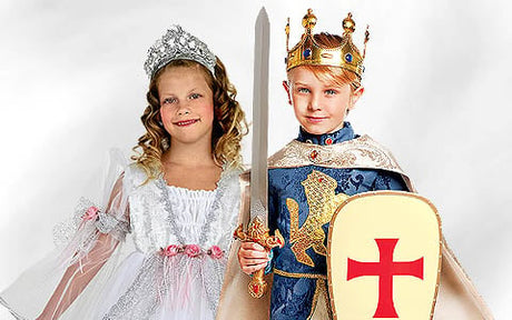 Ein Mädchen in einem weißen Prinzessinnenkleid und mit einer Krone steht neben einem Jungen in einem mittelalterlichen Königskostüm, der ein Schwert und einen Schild mit einem roten Kreuz in den Händen hält.