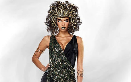 Eine Person in einem Medusa-Kostüm mit einem Kopfschmuck im Schlangen-Design, einem schwarzen Kleid und goldenem Armschmuck, die vor einem schlichten, hellen Hintergrund posiert.