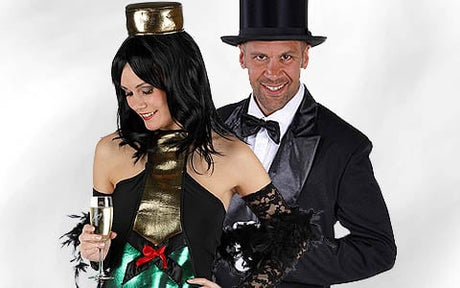 Zwei Erwachsene in Kostümen; die Frau trägt ein trägerloses schwarz-goldenes Kleid und hält ein Champagnerglas in der Hand, der Mann trägt einen schwarzen Smoking mit Zylinder, beide posieren gemeinsam.