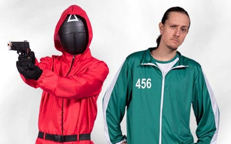 Zwei kostümierte Personen: eine in einem roten Overall und einer schwarzen Maske, bewaffnet mit einer Pistole, die andere in einem grünen Trainingsanzug mit der Nummer 456 – beide Anspielungen auf die Fernsehserie „Squid Game“..