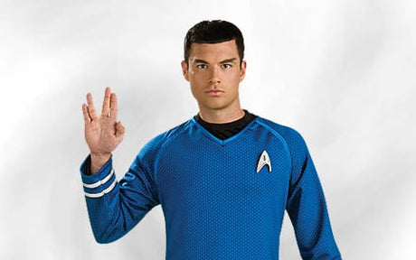 Eine Person in einer blauen „Star Trek“-Uniform hebt vor einem schlichten weißen Hintergrund die Hand zum vulkanischen Gruß.