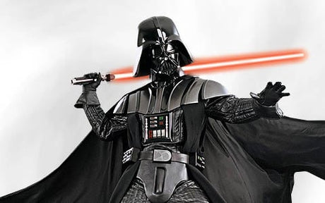 Eine Person mit schwarzem Helm und Rüstung steht vor einem schlichten Hintergrund und hält mit einer Hand ein rotes Lichtschwert, während sie die andere Hand ausstreckt.