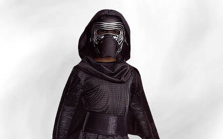 Eine Person, die eine schwarze Kapuzenrobe und eine metallische Maske trägt und vor einem schlichten, hellen Hintergrund steht.