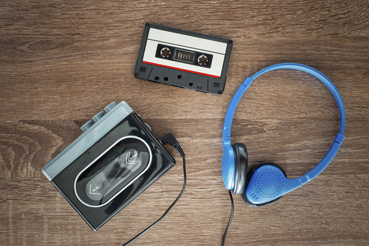 Auf einer Holzfläche liegen eine Kassette, ein tragbarer Kassettenplayer und blaue Kopfhörer.
