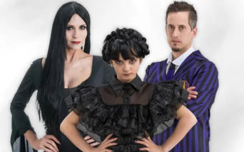 Drei Personen in schwarzer Kleidung im Gothic-Stil posieren gemeinsam; die Person vorne trägt ein Rüschenkleid, die beiden dahinter haben langes schwarzes Haar und tragen einen gestreiften Anzug.