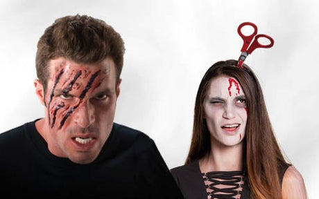 Zwei Personen mit Halloween-Make-up; der Mann hat künstliche Narben im Gesicht, und die Frau trägt ein Stirnband, das so aussieht, als steckten Scheren in ihrem Kopf – beide mit künstlichen Bluteffekten.