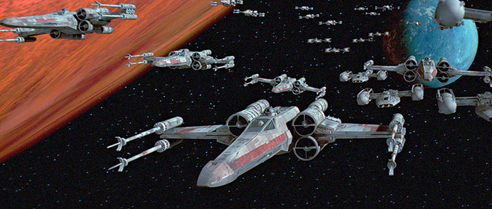 Eine Flotte von X-Wing-Sternjägern fliegt in Formation durch den Weltraum, links davon ist ein roter Planet zu sehen und im Hintergrund ein blauer Planet.