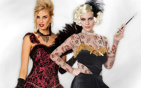Zwei Frauen tragen Kostüme im Vintage-Stil; die eine trägt ein rot-schwarzes Kleid mit einer Halskette, die andere ein schwarzes Kleid mit goldenen Verzierungen, einen Kopfschmuck mit Federn und hält eine Zigarettenspitze in der Hand.