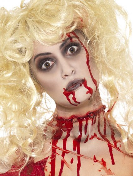 Eine Person mit einer blonden Perücke, auffälligem Make-up und Kunstblut im Gesicht und am Hals, was ihr ein gruseliges, an Horror angelehntes Aussehen verleiht.