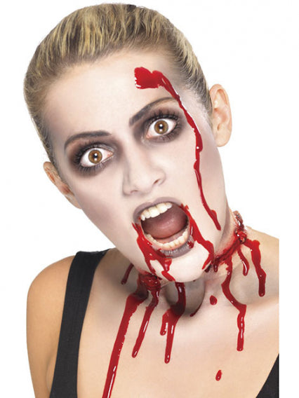 Eine Person mit blassem Make-up, dunklem Lidschatten und Kunstblut im Gesicht und am Hals, die eine Kehlwunde zu haben scheint, die an Halloween oder ein Horrorthema erinnert.