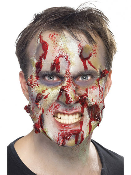 Eine Person mit realistischem Zombie-Make-up, das künstliche Wunden, Blut und verfaulte Haut zeigt, starrt geradeaus und fletscht die Zähne.