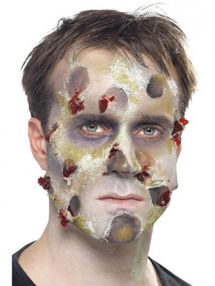 Ein Mann mit Spezialeffekt-Make-up, das verwesende, zombieähnliche Haut mit Wunden und Verfärbungen im Gesicht darstellt, blickt direkt in die Kamera.