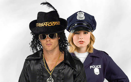 Ein Mann in einem Rockstar-Kostüm mit Sonnenbrille und eine Frau in einem Polizistenkostüm stehen nebeneinander vor einem einfarbigen Hintergrund.