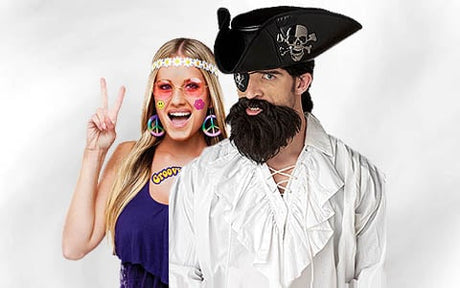 Eine Frau in einem Hippie-Kostüm steht neben einem Mann in einem Piratenkostüm mit schwarzem Hut und Bart; beide posieren vor einem weißen Hintergrund.